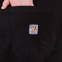 Back pocket close up of Original Overalls in Mono Black. Catie has her hand in the pocket.