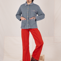 Railroad Stripe Denim Work Jacket and paprika Western Pants worn by Jesse. They have both hands in the front pockets of jacket.