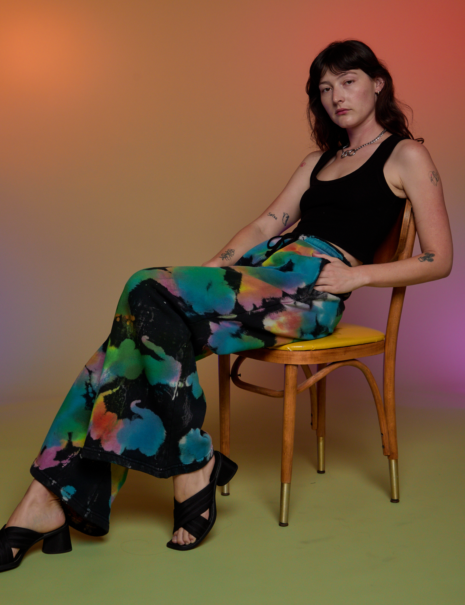 Alex is wearing Tie Dyed Wide Leg Sweat Pants and black Tank Top sitting in a chair