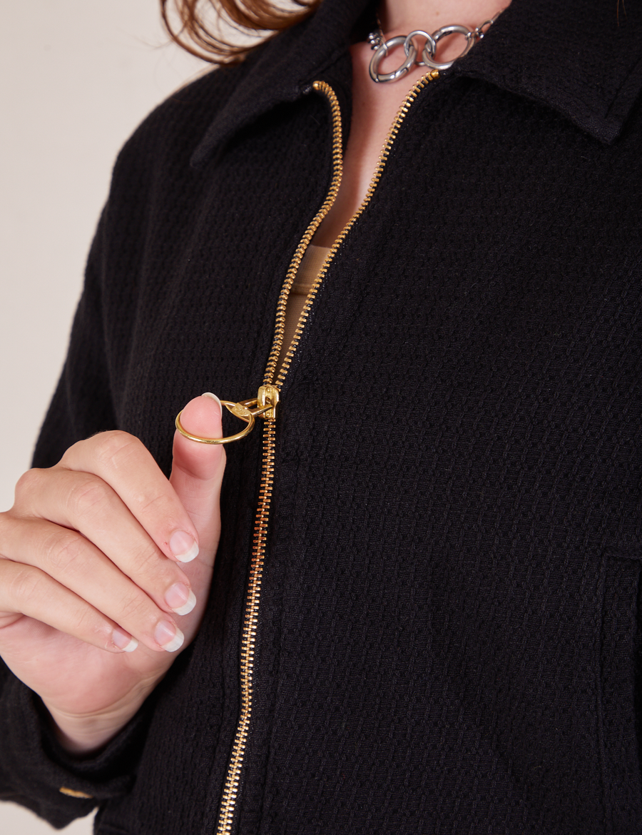 Front close up of Ricky Jacket in Basic Black featuring brass zipper. Alex has her thumb in the ring of the zipper pull