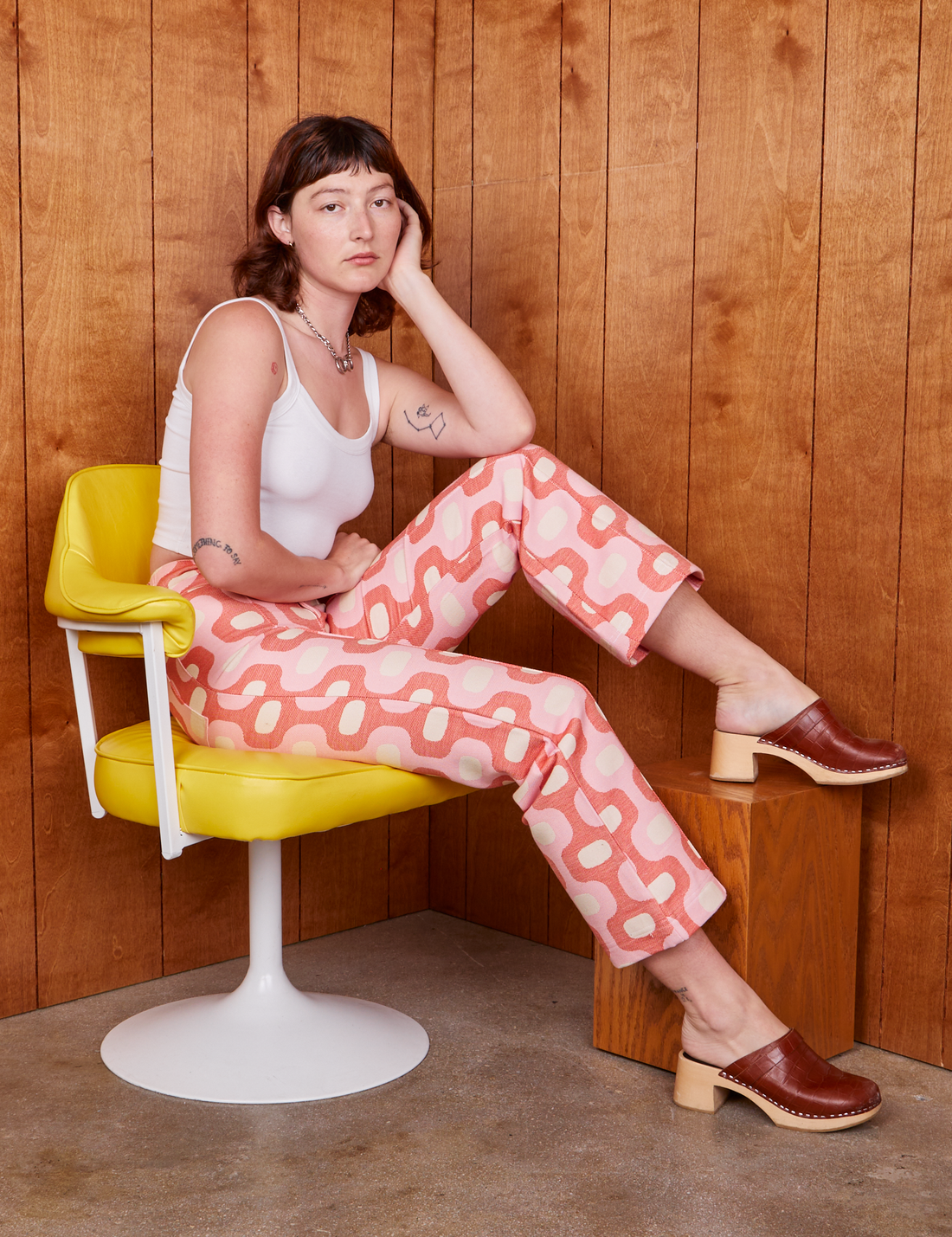 Alex is sitting on a yellow chair wearing Western Pants in Pink Jacquard
