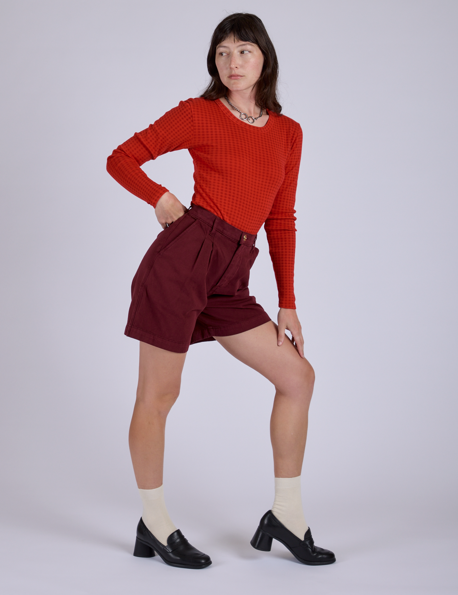 Side view of Pleated Trouser Shorts in Red Wine and mustang red Long Sleeve Gingham Baby Tee on Alex