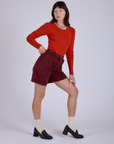 Side view of Pleated Trouser Shorts in Red Wine and mustang red Long Sleeve Gingham Baby Tee on Alex