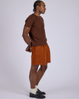Side view of Pleated Trouser Shorts in Burnt Terracotta and fudgesicle brown Organic Vintage Tee on Jerrod