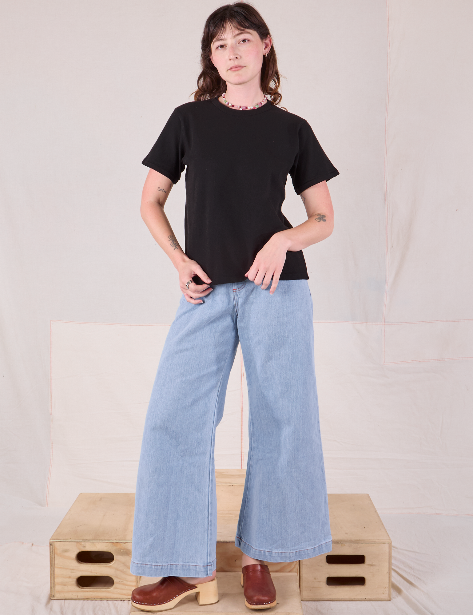 Alex is wearing Burly Tee in Basic Black paired with light wash Denim Wide Leg Trousers