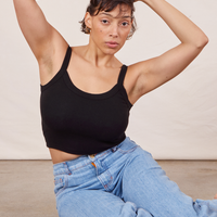 Tiara is sitting on the concrete floor wearing Cropped Cami in Basic Black and light wash Sailor Jeans