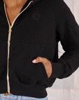 Cropped Zip Hoodie in Basic Black front close up. Kandia has her hand in the pocket.