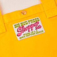 Sun Baby brass snap on Sunshine Yellow Shopper Tote Bag. Bag label in green and pink text that reads "Big Bud Press, Shopper Tote, Made in L.A., 100% Cotton Denim" on a white background