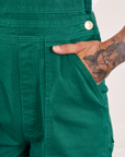 Front pocket close up of Original Overalls in Mono Hunter Green. Jesse has their hand in the pocket.