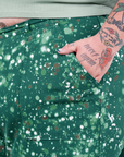 Front pocket close up of Marble Splatter Work Pants in Hunter Green. Sam has their hand in the pocket.