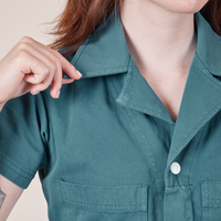 Upper front close up of Petite Short Sleeve Jumpsuit in Marine Blue. Hana is holding the point of a collar.