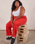 Morgan is sitting on a stack of wooden crates wearing Work Pants in Mustang Red