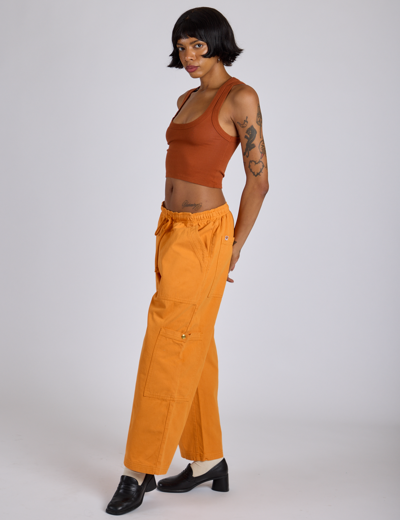 Side view of Drop Pocket Cargo Pants in Creamsicle Orange and burnt terracotta Cropped Tank on Kira