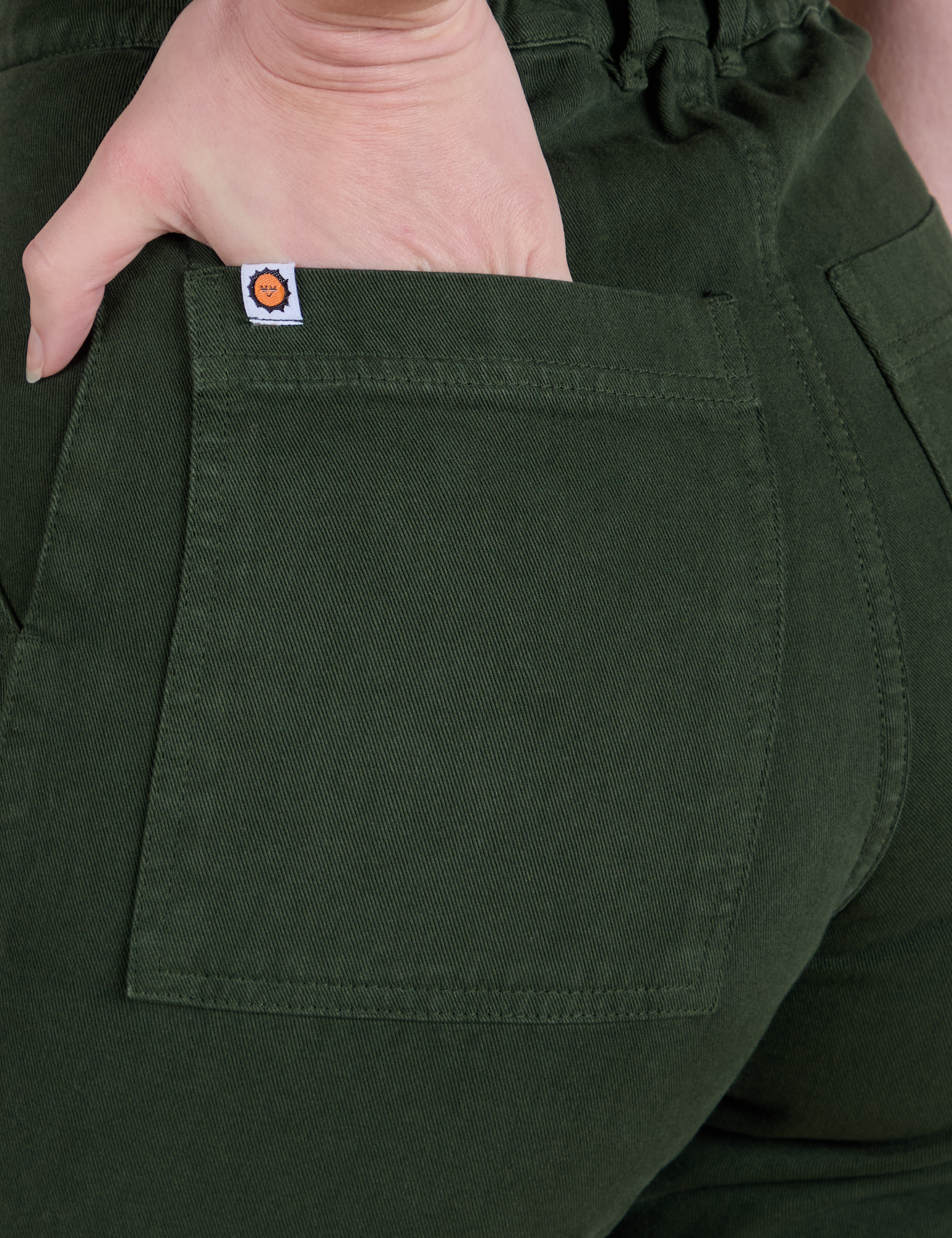 Close up of Alex's hand in the back pocket of Short Sleeve Jumpsuit in Swamp Green