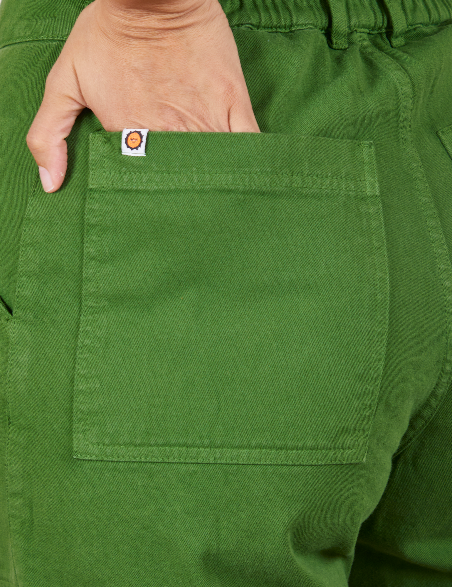 Back pocket close up of Short Sleeve Jumpsuit in Lawn Green. Tiara has her hand in the pocket.