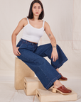 Betty is sitting on a wooden crate. They are wearing Indigo Wide Leg Trousers in Dark Wash and vintage off-white Cami.