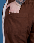 Close up of Sydney's hand in the back pocket of Painted Action Pants in Fudgesicle Brown
