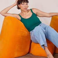Tiara is sitting on an orange upholstered chair wearing Cropped Cami in Hunter Green and light wash Frontier Jeans