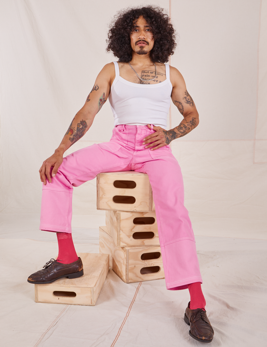 Jesse is sitting on a stack of wooden crates. They are wearing Carpenter Jeans in Bubblegum Pink and vintage off-white Cami