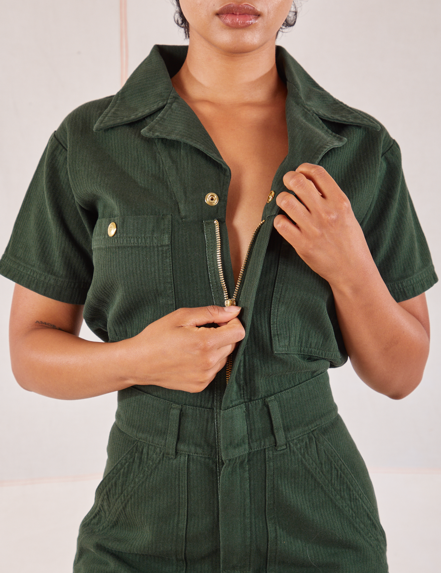 Heritage Short Sleeve Jumpsuit in Swamp Green close up. Mika is pulling down the zipper