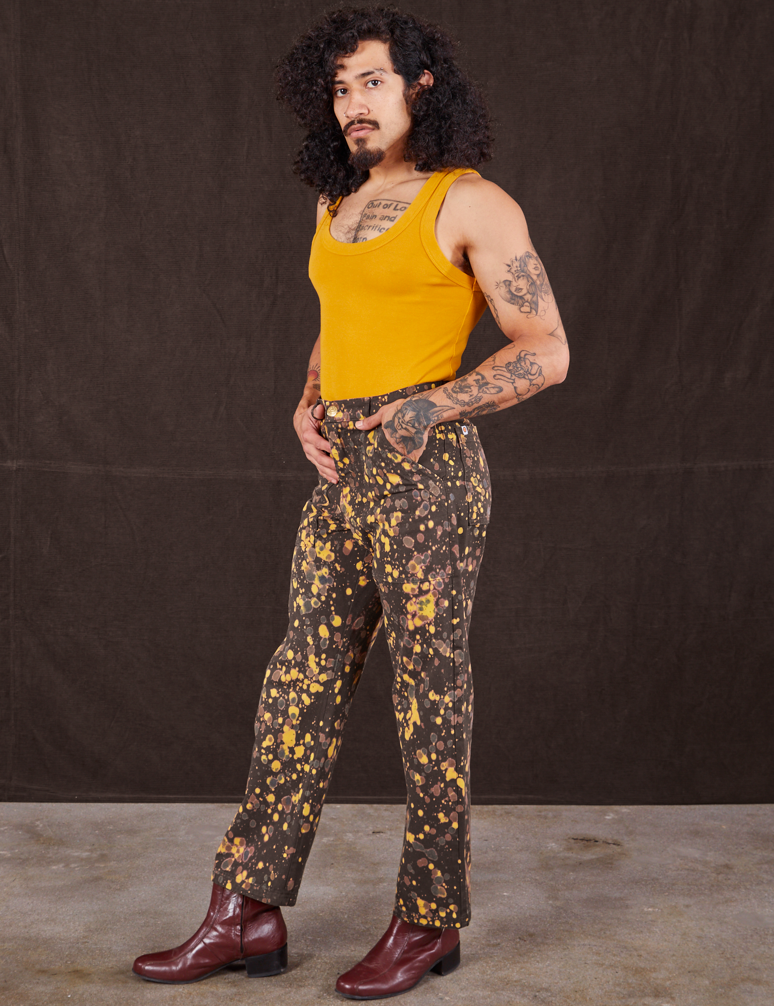 Angled front view of Marble Splatter Work Pants in Espresso Brown and mustard yellow Tank Top on Jesse