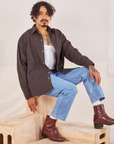 Jesse is sitting on a wooden crate. They are wearing Oversize Overshirt in Espresso Brown, vintage off-white Cropped Tank Top and light wash Frontier Jeans