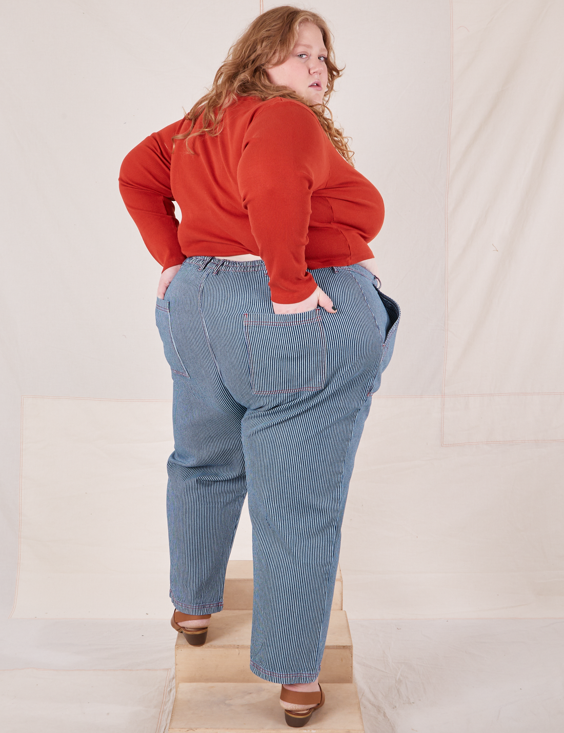 Back view of Railroad Stripe Denim Work Pants and paprika Long Sleeve V-Neck Tee worn by Catie. 