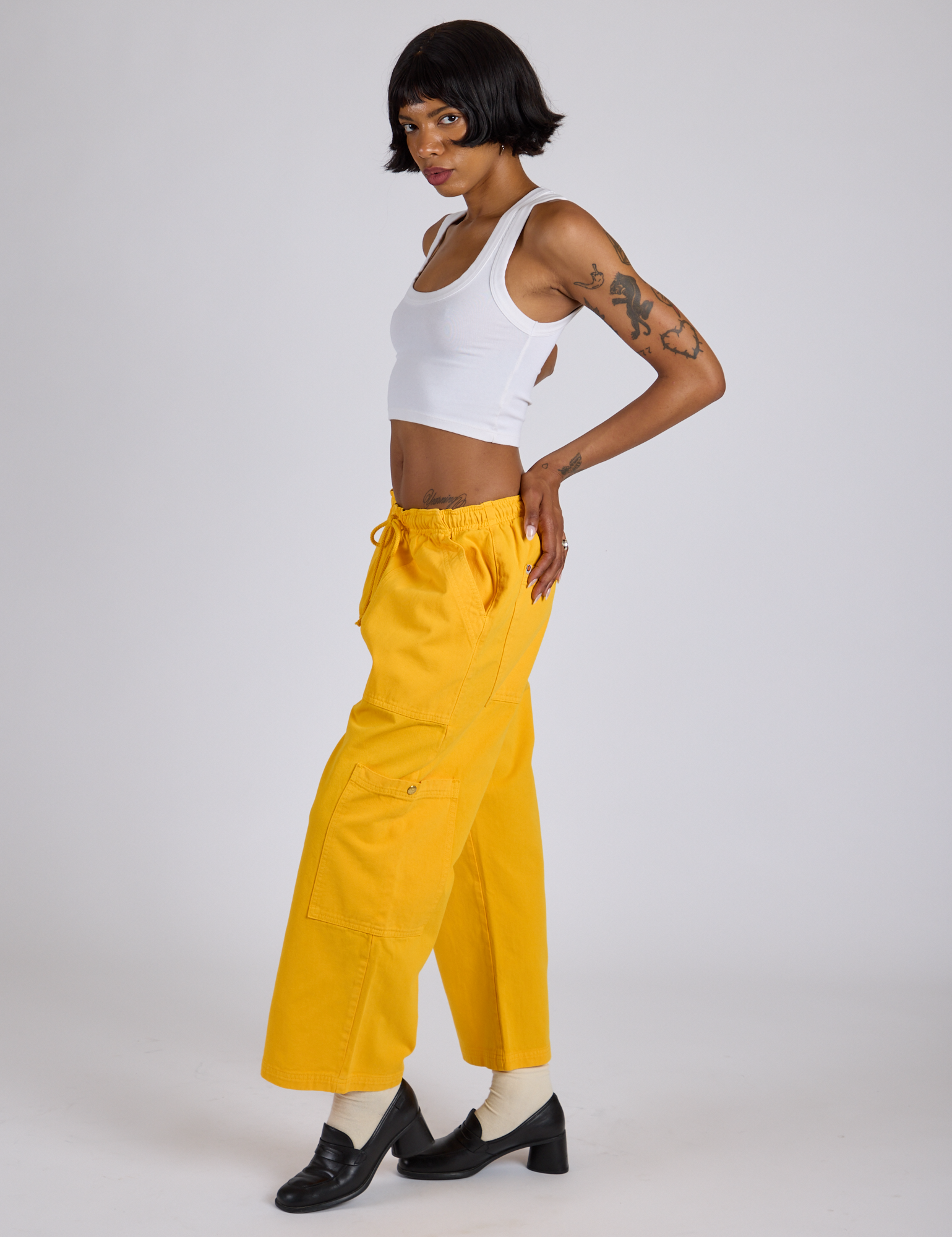 Side view of Drop Pocket Cargo Pants in Sunshine Yellow and Cropped Tank in Vintage Tee White on Kira