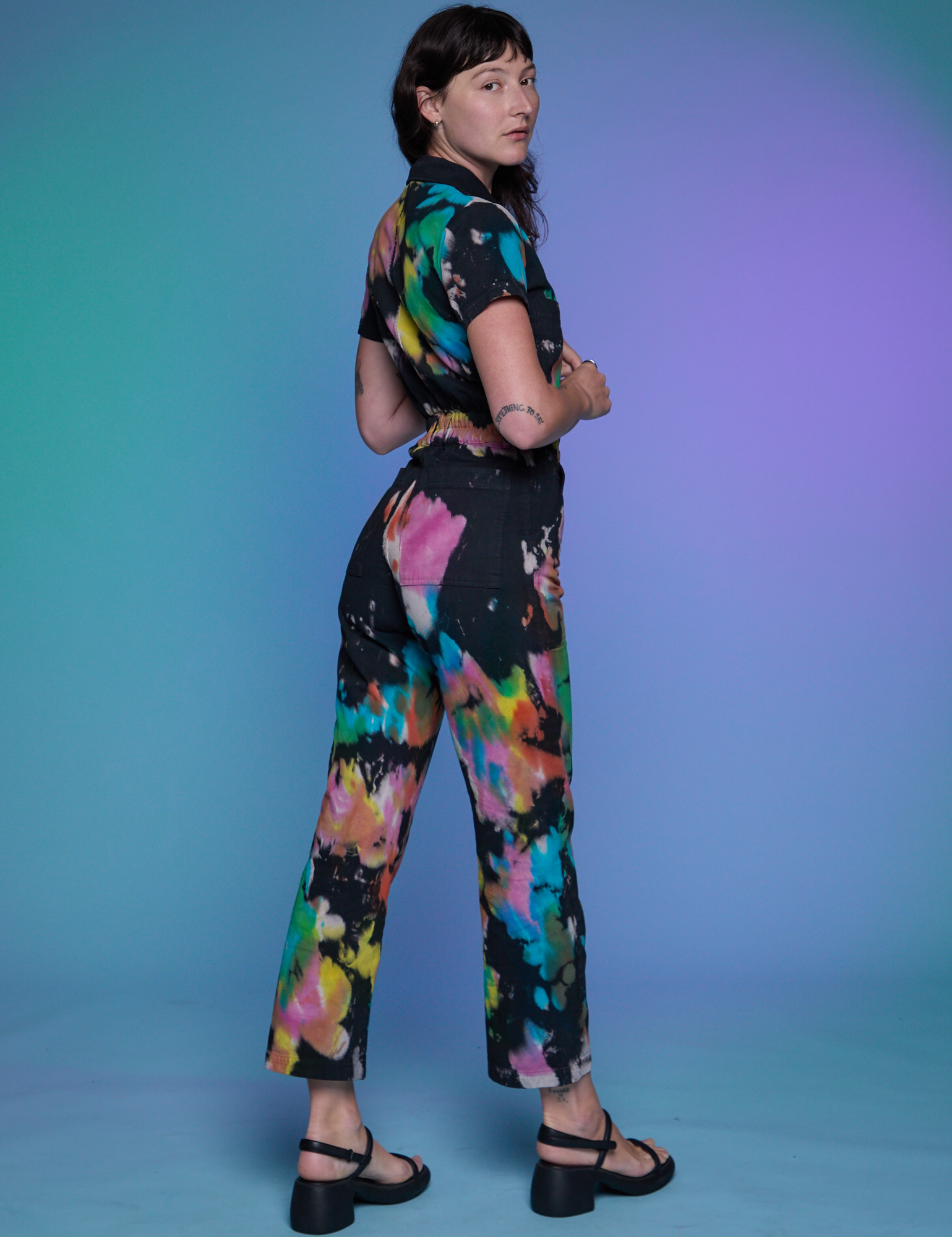 Angled back view of Short Sleeve Jumpsuit in Rainbow Magic Waters on Alex