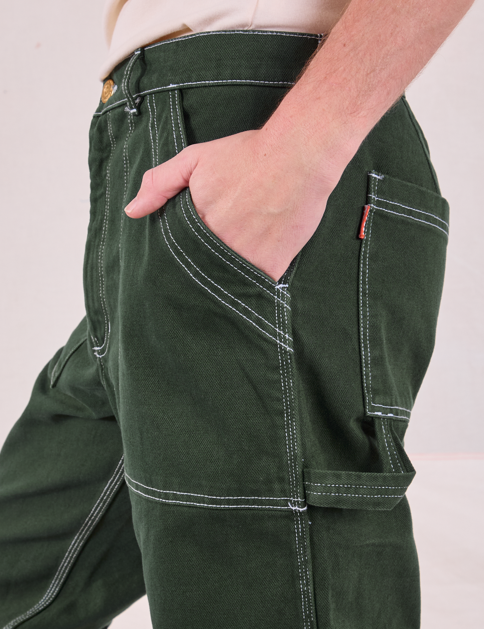 Close up of Quinn&#39;s hand in the front pocket of Carpenter Jeans in Swamp Green