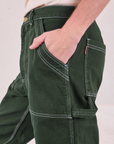 Close up of Quinn's hand in the front pocket of Carpenter Jeans in Swamp Green