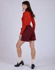 Angled back view of  Pleated Trouser Shorts in Red Wineand mustang red Long Sleeve Gingham Baby Tee on Alex