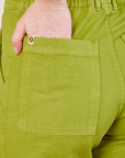 Work Pants in Gross Green back pocket close up.  Margaret has her hand in the pocket.