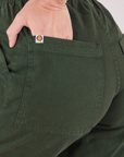 Action Pants in Swamp Green back pocket close up. Alex has her hand in the pocket.