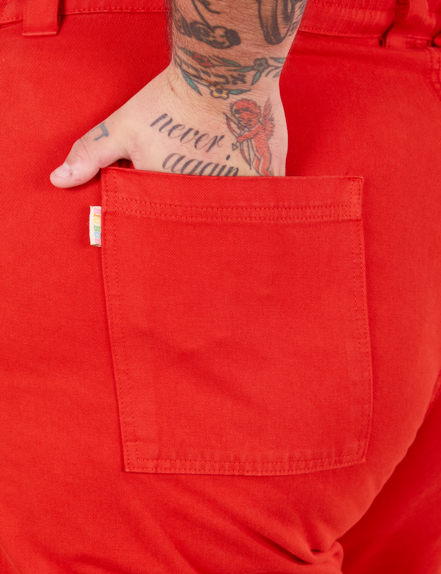 Bell Bottoms in Mustang Red back pocket close up. Sam has their hand in the pocket.