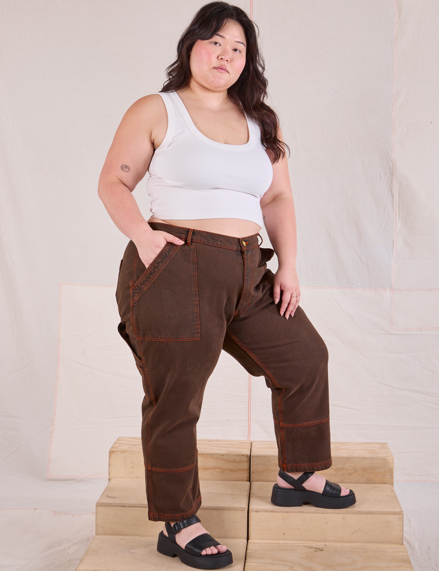 Angled front view of Overdyed Carpenter Jeans in Fudge and Cropped Tank in vintage tee off-white on Ashley