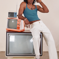 Three vintage tvs are stacked on top of each other. Jerrod is sitting on the large tv with his right elbow on a smaller orange and white tv. They are wearing Cropped Cami in Marine Blue and vintage off-white Western Pants.