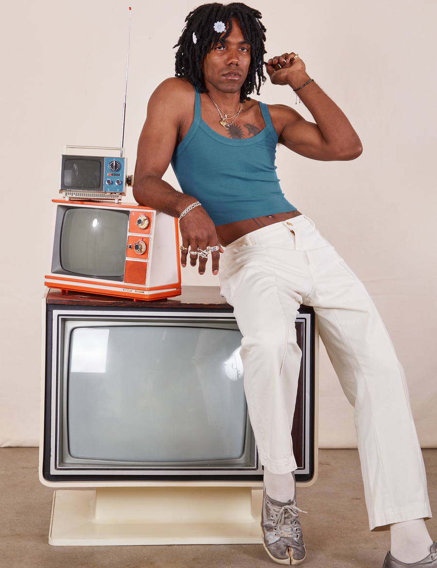 Three vintage tvs are stacked on top of each other. Jerrod is sitting on the large tv with his right elbow on a smaller orange and white tv. They are wearing Cropped Cami in Marine Blue and vintage off-white Western Pants.