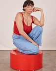 Tiara is kneeling on a red circular platform wearing Cropped Cami in Mustang Red and light wash Western Pants