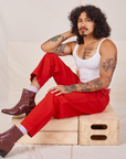 Jesse is sitting on a wooden crate. They are wearing Heavyweight Trousers in Mustang Red and vintage off-white Cropped Cami.