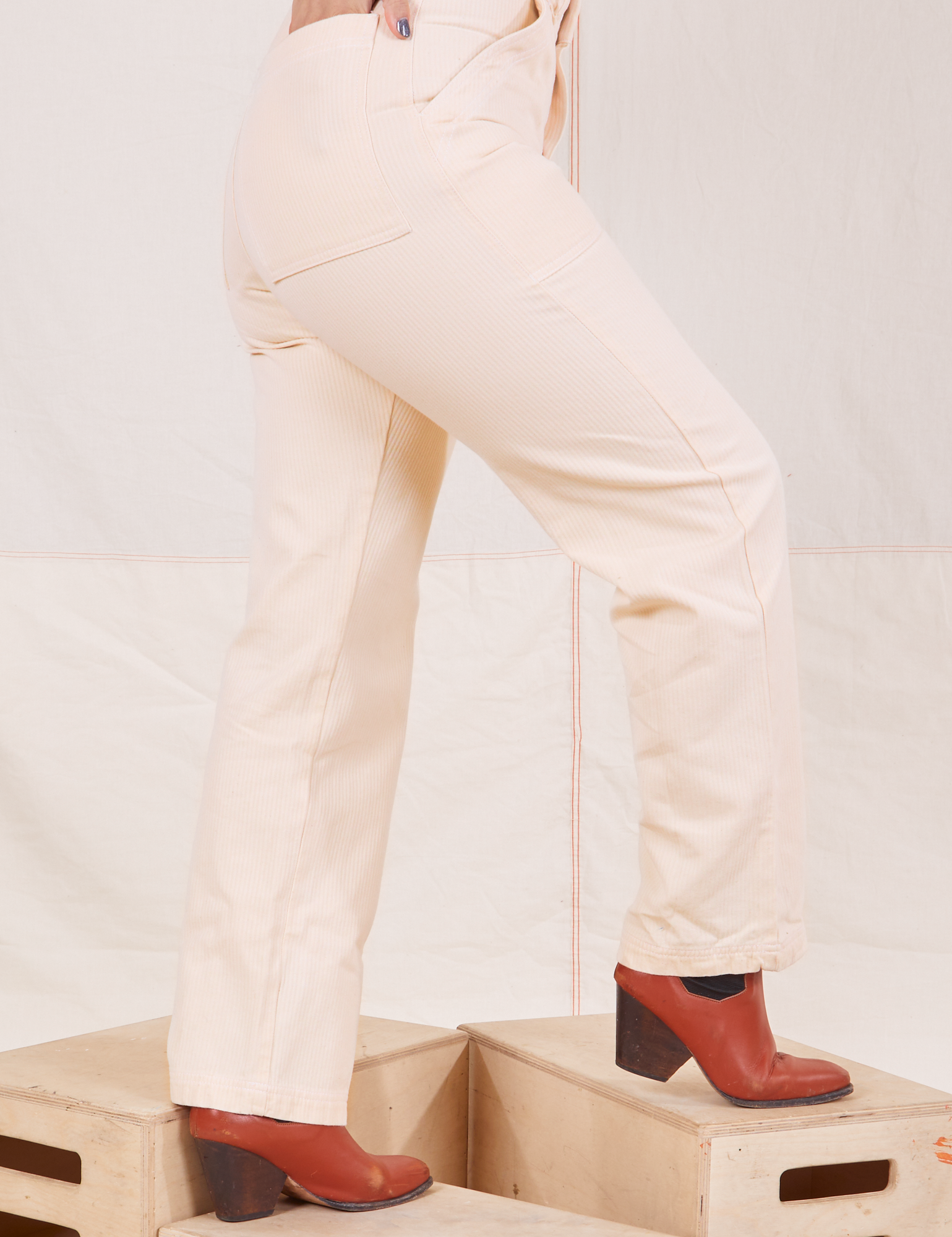 Heritage Short Sleeve Jumpsuit in Vintage Off-White side view close up of pant legs. Worn by Tiara with hand in back pocket.