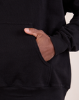 Oversized Hoodie in Basic Black front pocket close up. Issac has his hand in the pocket.