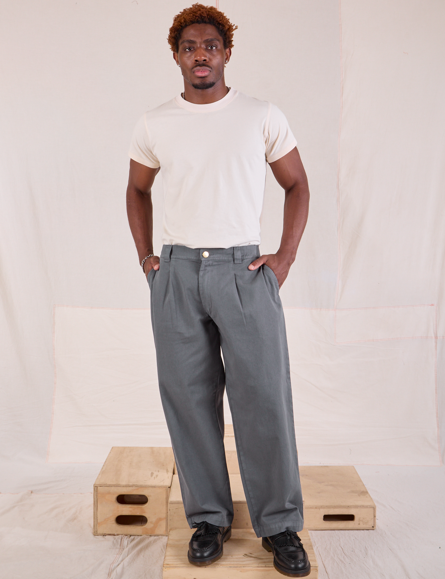 Issac is 5&#39;10&quot; and wearing M Mid-Rise Pleated Trousers in Slate Grey paired with Organic Vintage Tee in vintage tee off-white