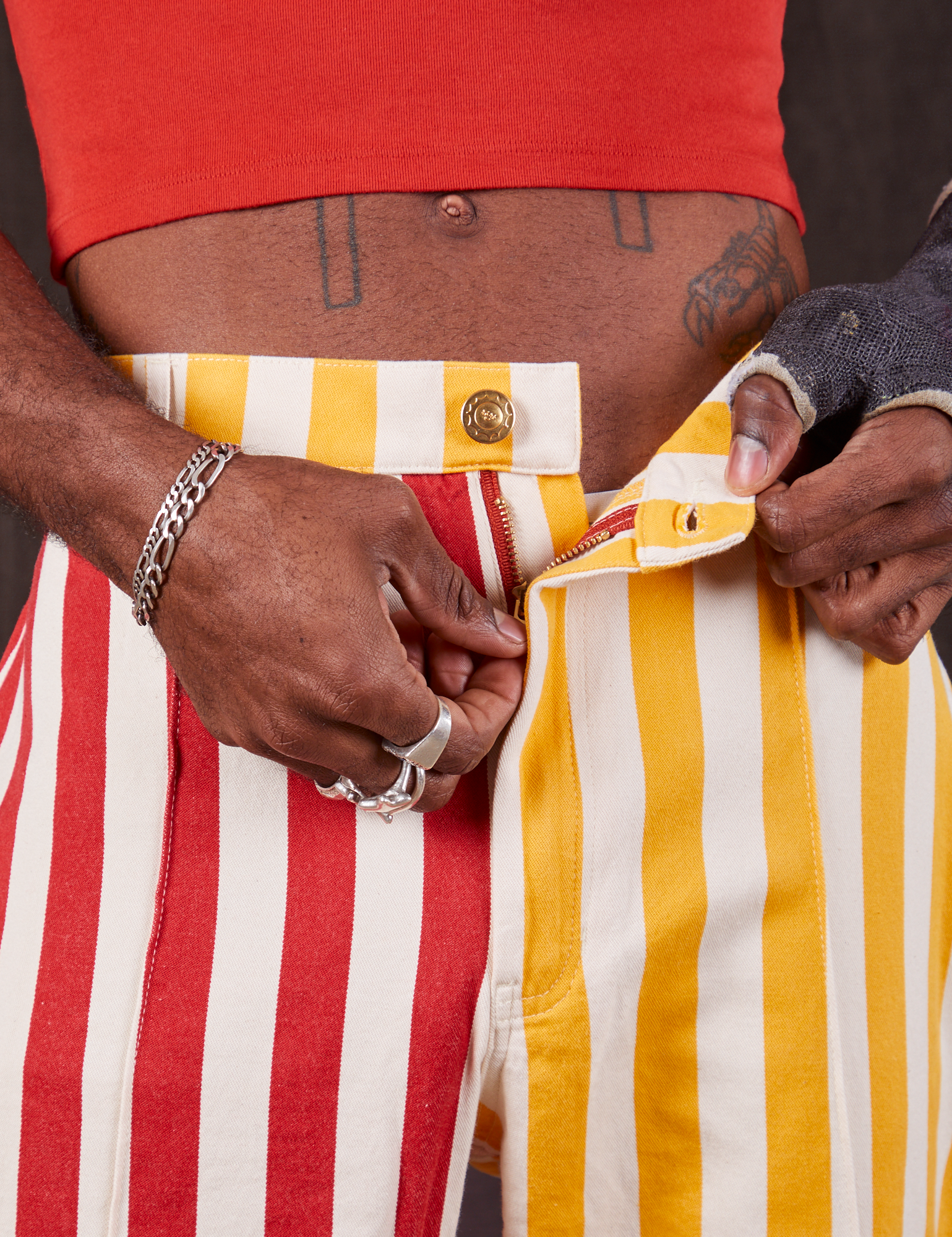 Western Pants in Ketchup/Mustard Stripes front close up. Jerrod is pulling the zipper tab down.