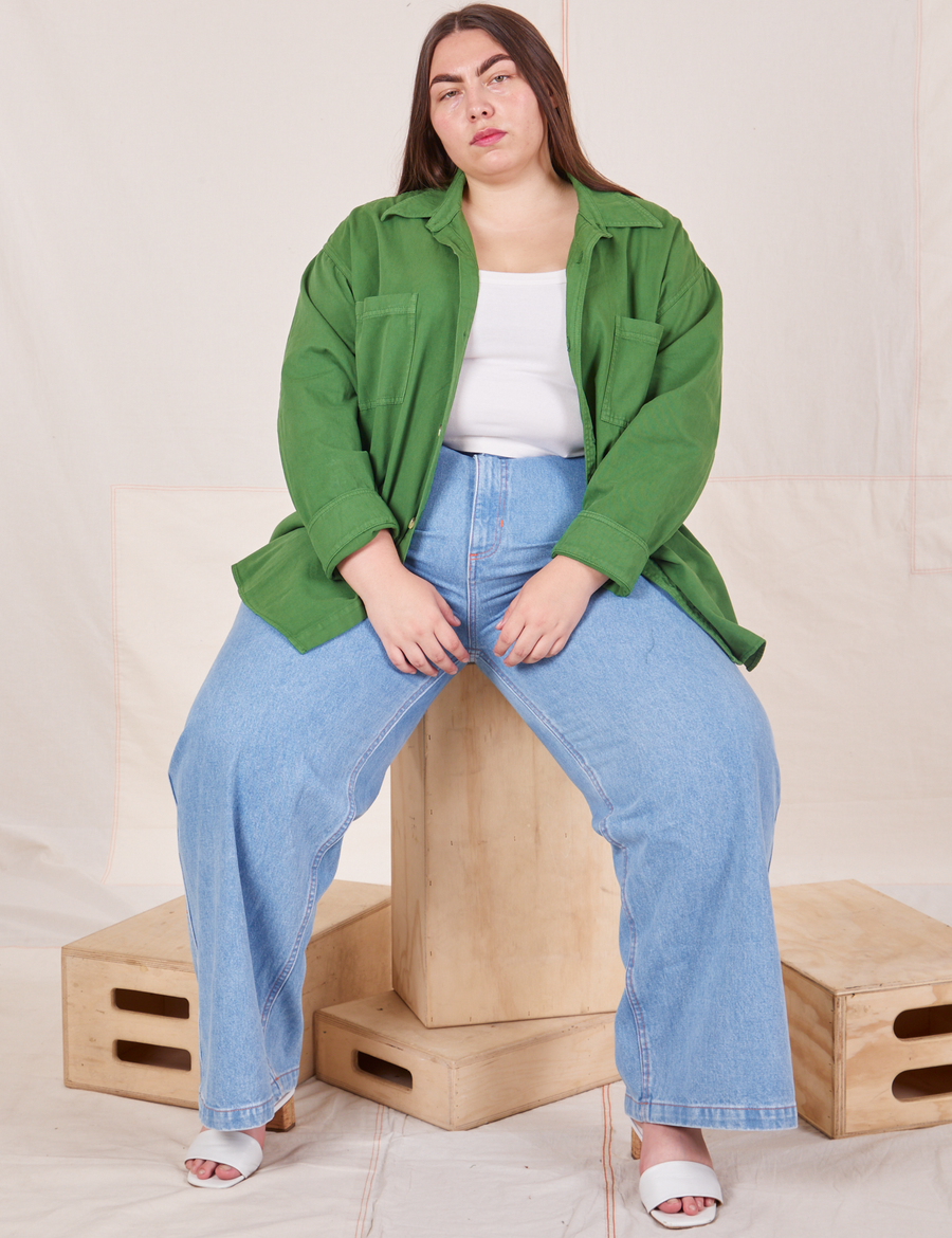 Marielena is sitting on a wooden crate wearing Oversize Overshirt in Lawn Green paired with vintage off-white Cropped Tank Top and light wash Sailor Jeans