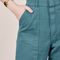 Front pocket close up of Petite Short Sleeve Jumpsuit in Marine Blue. Hana has her hand in the pocket.