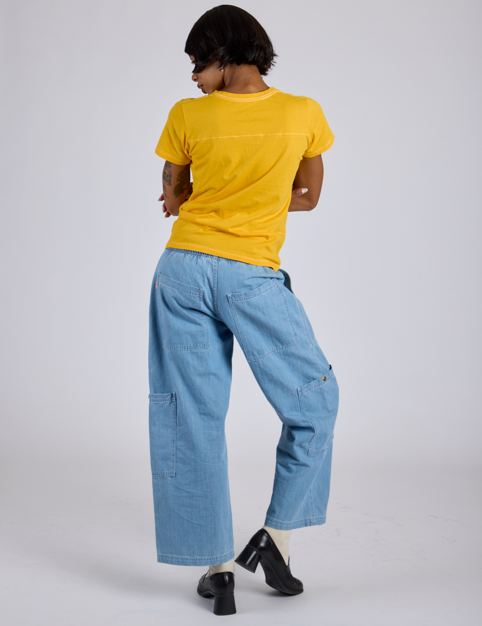 Back view of Jr. Varsity Tee in Sunshine Yellow and light wash Denim Drop Pocket Pants on Kira