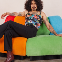 Jesse is sitting on an upholstered chair wearing Cropped Cami in Rainbow Magic Waters and black Western Pants