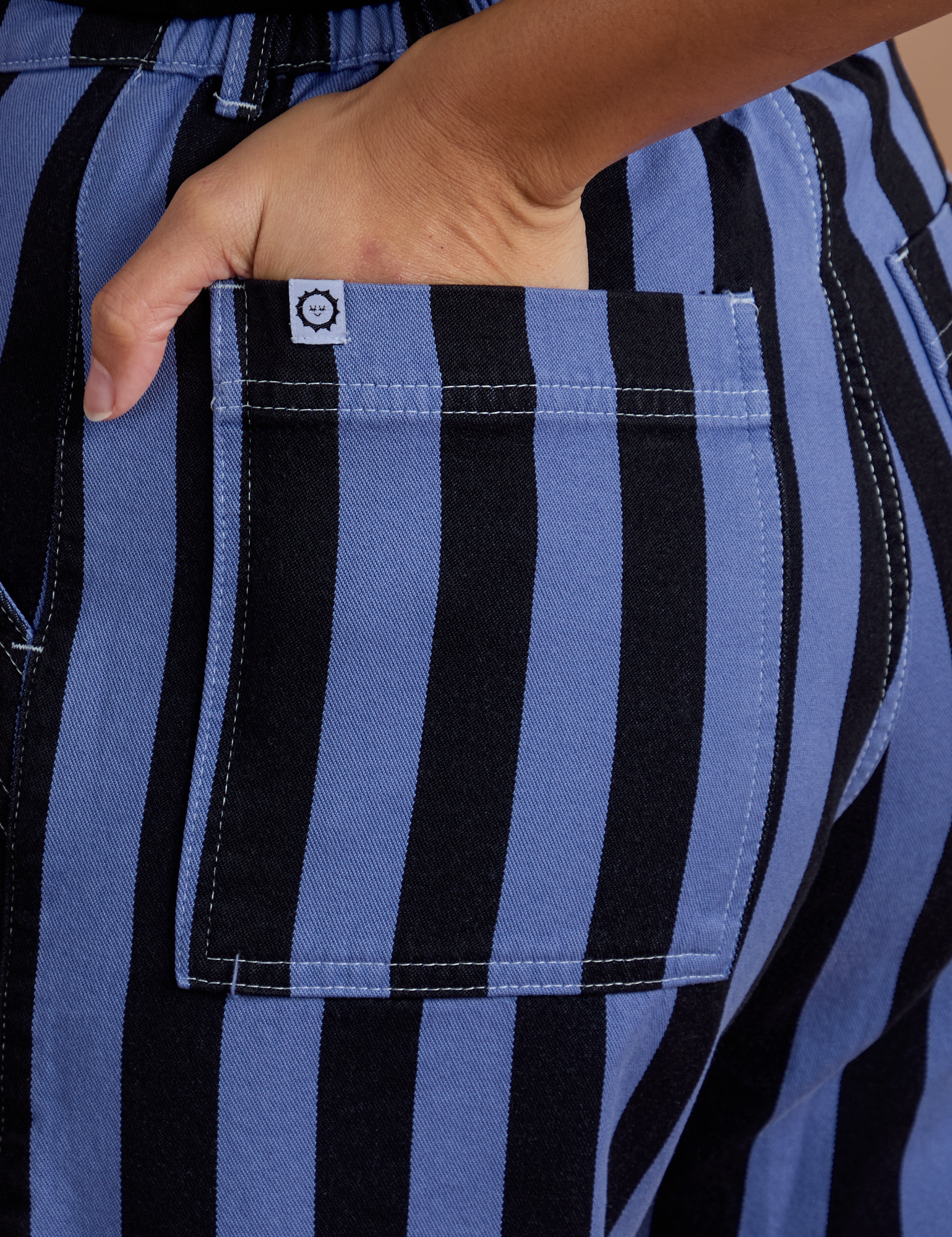 Close up of Tiara's hand in the back pocket of Black Stripe Work Pants in Cornflower Blue
