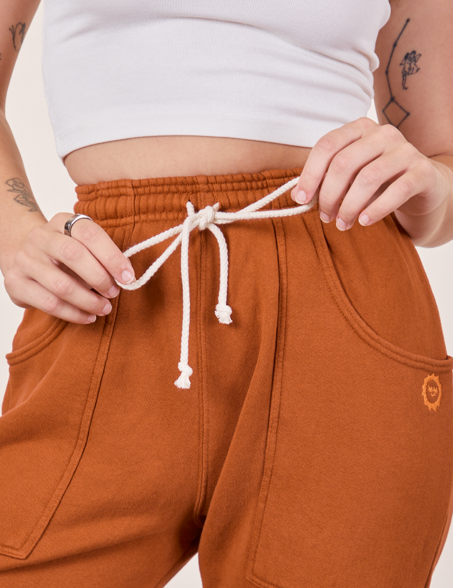 Cropped Rolled Cuff Sweatpants in Burnt Terracotta front close up. Alex is holding onto the drawstring